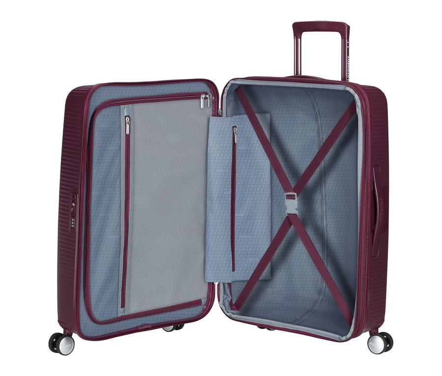 Offener American Tourister Hartschalen-Koffer »Soundbox« Spinner, mittel, in Wildkirschrot. Die linke Seite zeigt eine Netztrennwand mit Reißverschluss, die rechte Seite hat Packgurte und eine ausziehbare Teleskopstange.