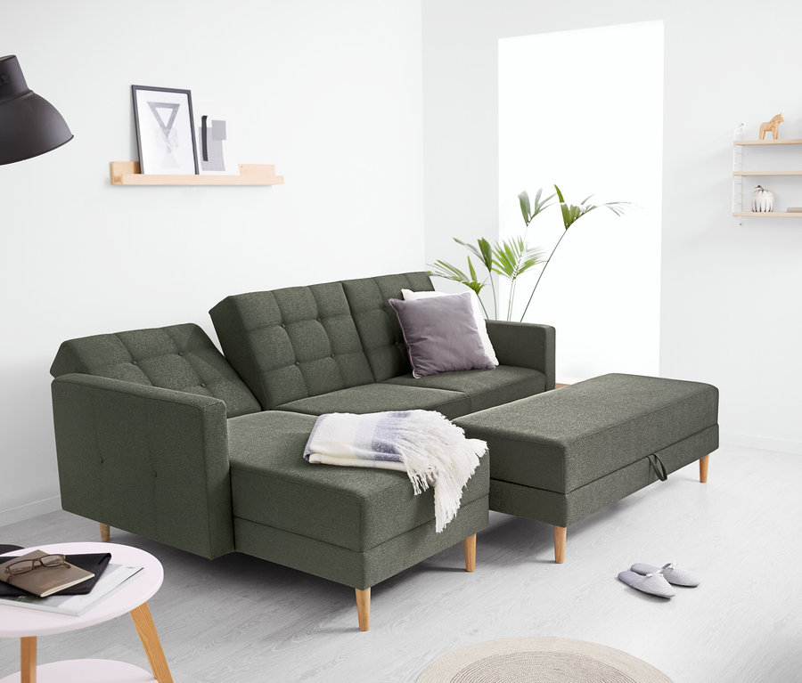 Grünes Federkern-Eckschlafsofa »Just Relax« mit Stauraumbank in einem hellen Wohnzimmer mit Stehlampe, Beistelltisch und Wandregalen.