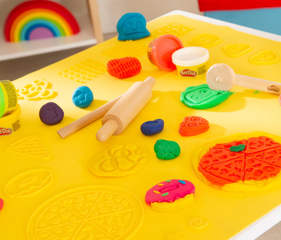 Nahaufnahme von Play-Doh und Werkzeugen auf einem gelben roba x Play-Doh Sitzgruppen-Set Tisch. Regenbogen im Hintergrund.