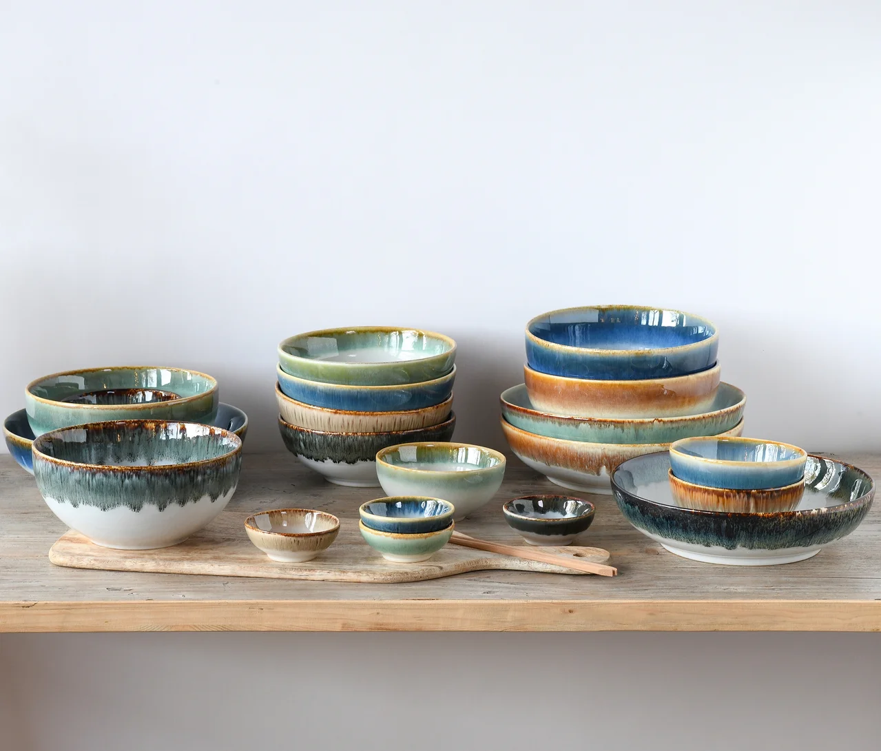 creaTable Bowl-Set »Cascade«: Verschiedene Keramikschalen mit reaktiver Glasur in Blau-, Grün- und Brauntönen, auf einem Holzbrett arrangiert.