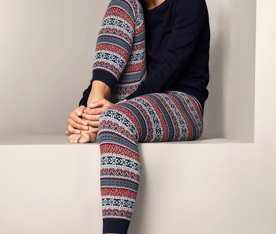Lächelnde Frau sitzt und trägt eine Strickleggings im Norweger-Dessin und ein marineblaues Oberteil.