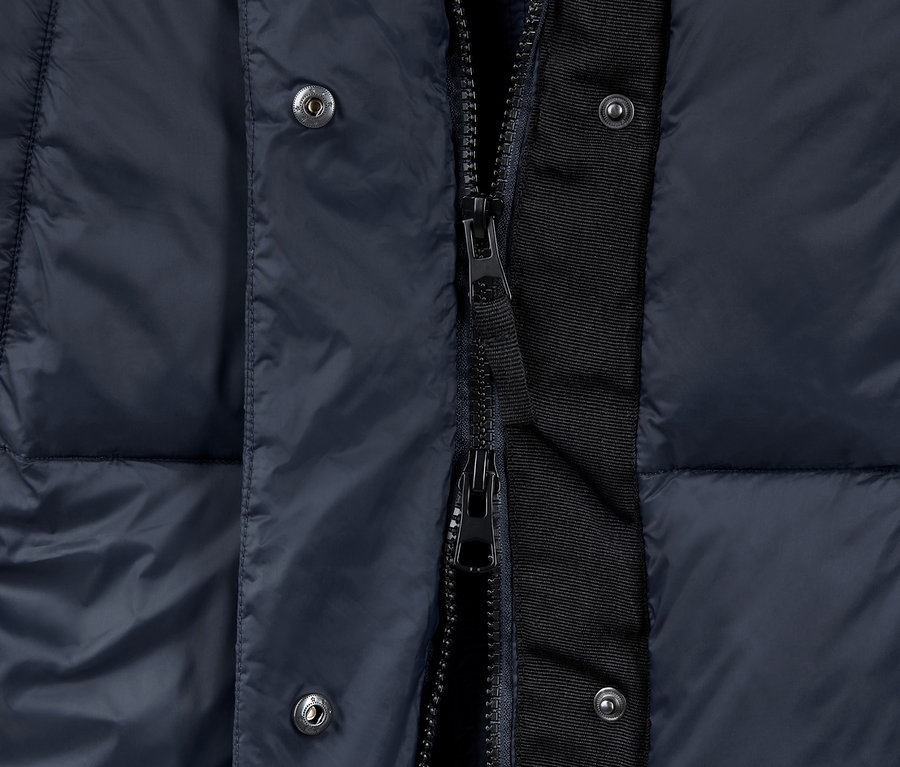 Detailaufnahme einer langen, gesteppten, marineblauen Weste mit Reißverschluss und Knöpfen.