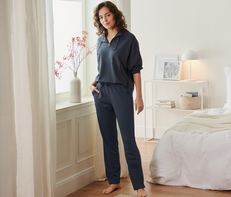 Frau steht im Raum am Fenster und trägt eine Piqué-Loungehose.