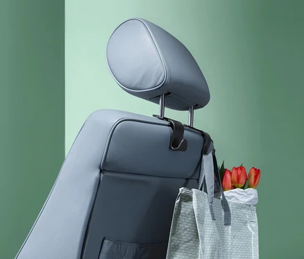 Auf der Kopfstütze eines grauen Autositzes hängen 2 Kopfstützen-Haken, an denen eine Einkaufstasche mit roten Tulpen hängt.
