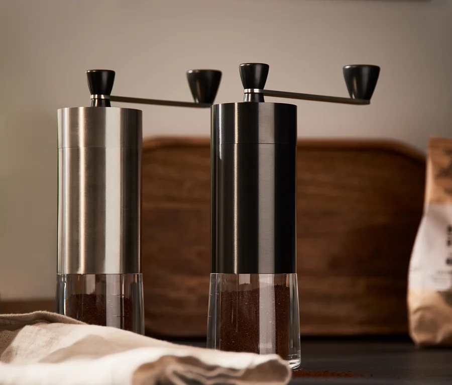 Zwei Kaffeemühlen, eine silberne und eine schwarze, stehen nebeneinander auf einem Tisch.