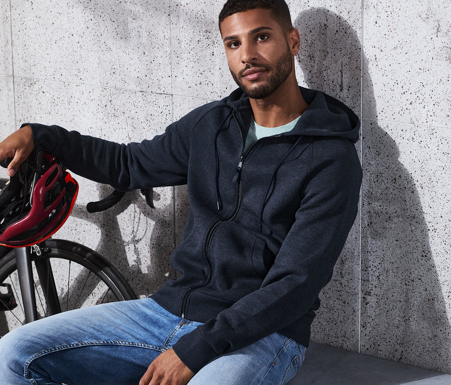 Mann sitzt neben einem Fahrrad und hält einen Helm, er trägt eine Funktionsjacke.