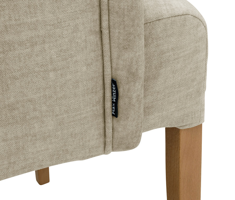 Detailansicht eines beigen »Hendrick« Polsterstuhls mit Armlehne und einem Holzbein.