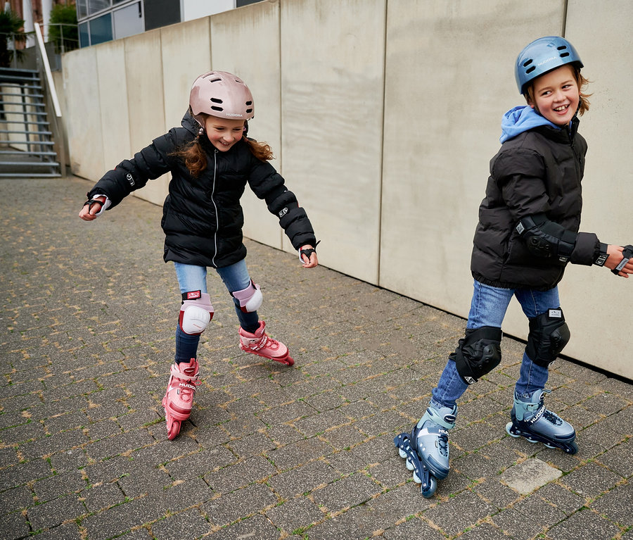 Zwei Kinder fahren mit HUDORA Inline Skates Mia 2.0 und Leon 2.0 und Schützern.