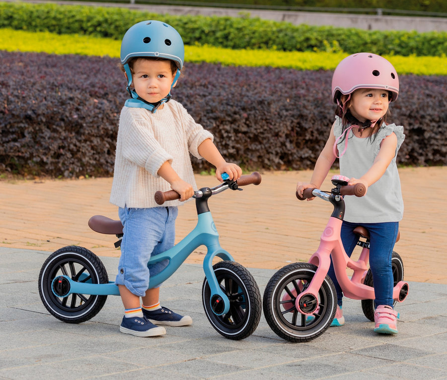 Ein Junge und ein Mädchen mit Helmen stehen nebeneinander und halten die Lenker von GLOBBER GO Laufrädern »Elite Air« in Pastellblau und Rosa.