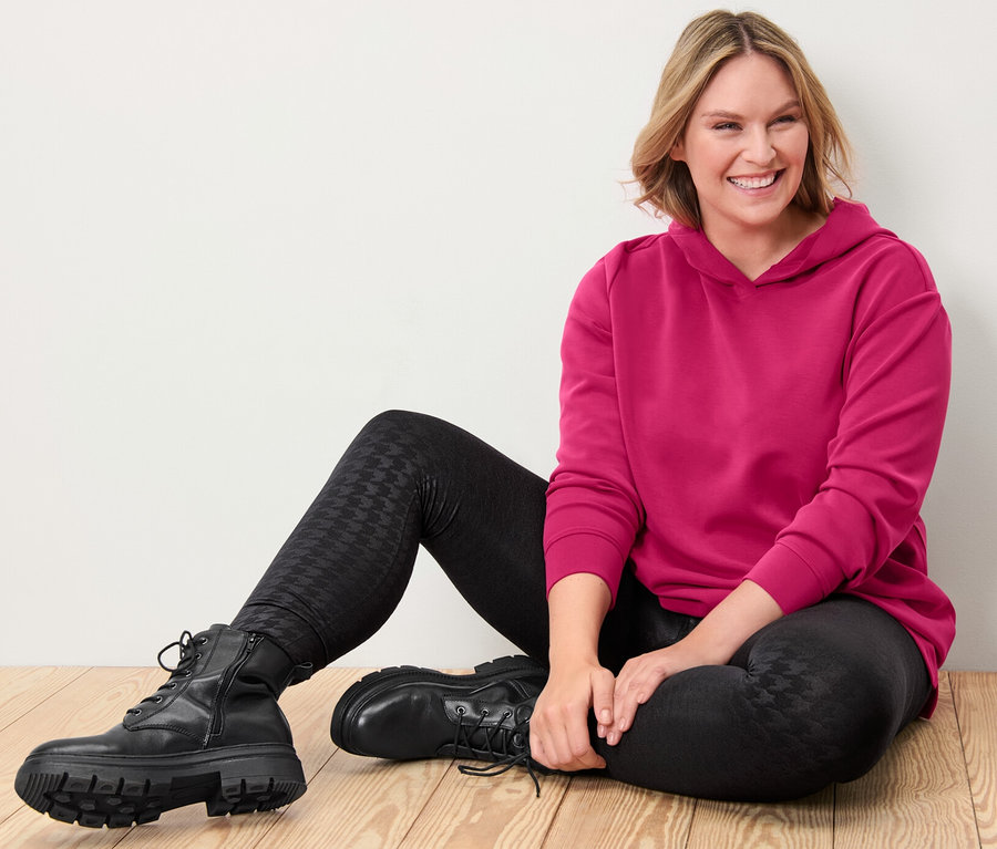 Frau sitzt auf Holzboden, trägt einen pinken Hoodie aus Modal-Mix und Thermoleggings mit Prägung.