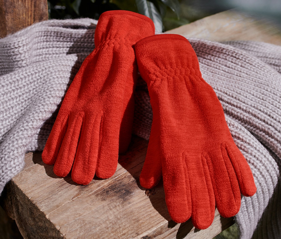 Orange Fleece-Handschuhe liegen auf einem Strickschal auf einer Holzbank.