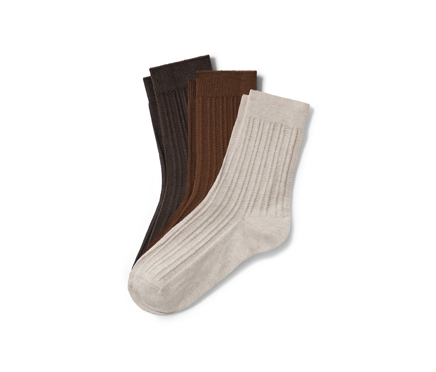 Drei Paar Socken mit Zopfmuster in Braun-, Hellbraun- und Beigetönen liegen auf einem weißen Hintergrund.