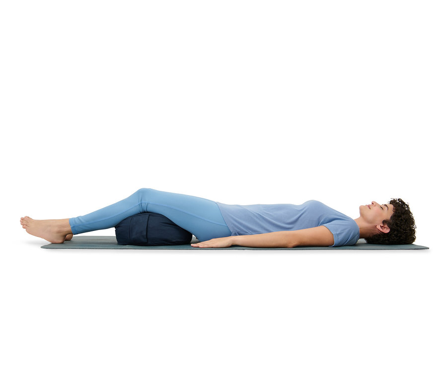 Frau liegt auf einer Matte, die Beine auf einem Meditationskissen.