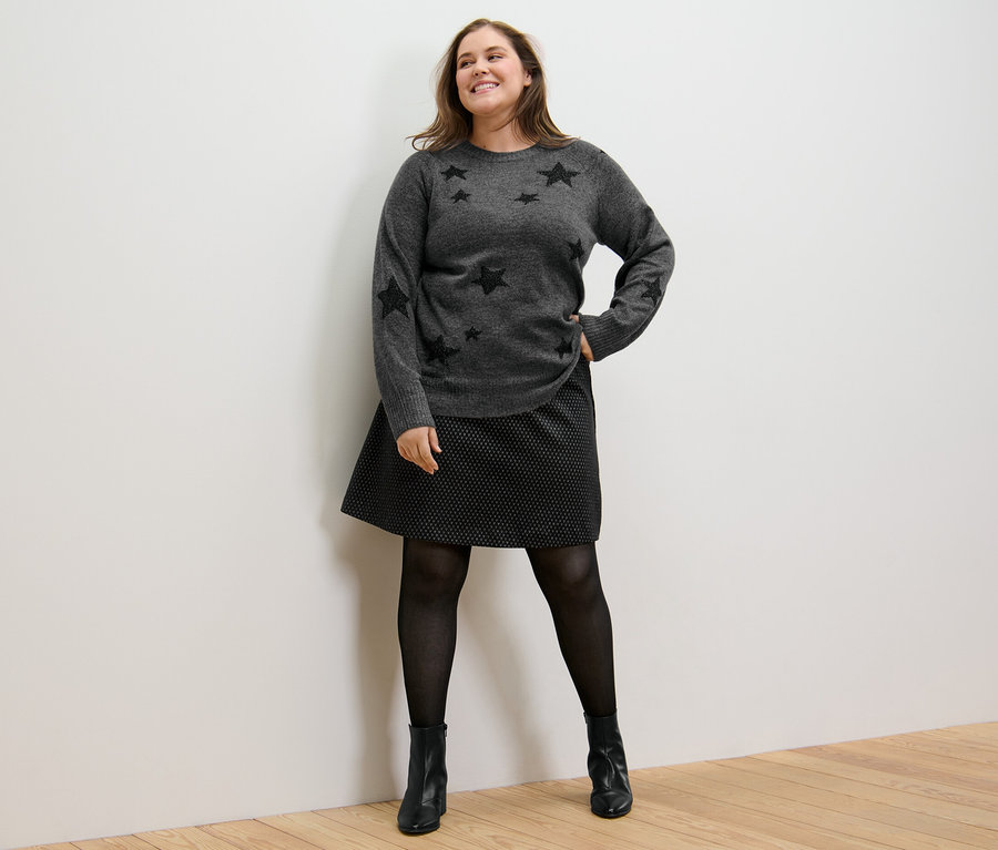 Frau posiert in Strickpullover und glitzerndem Jacquard-Rock.