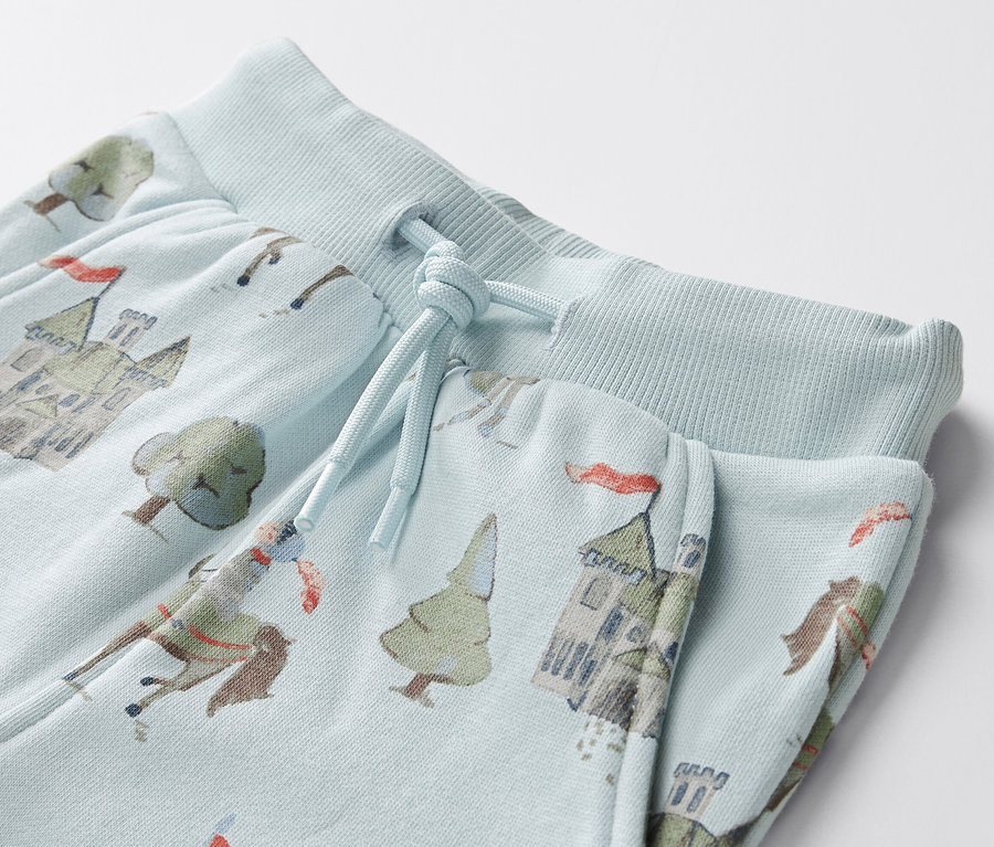 Detailansicht von hellblauen Baby-Sweathosen mit Ritter-, Burg- und Baumprint.