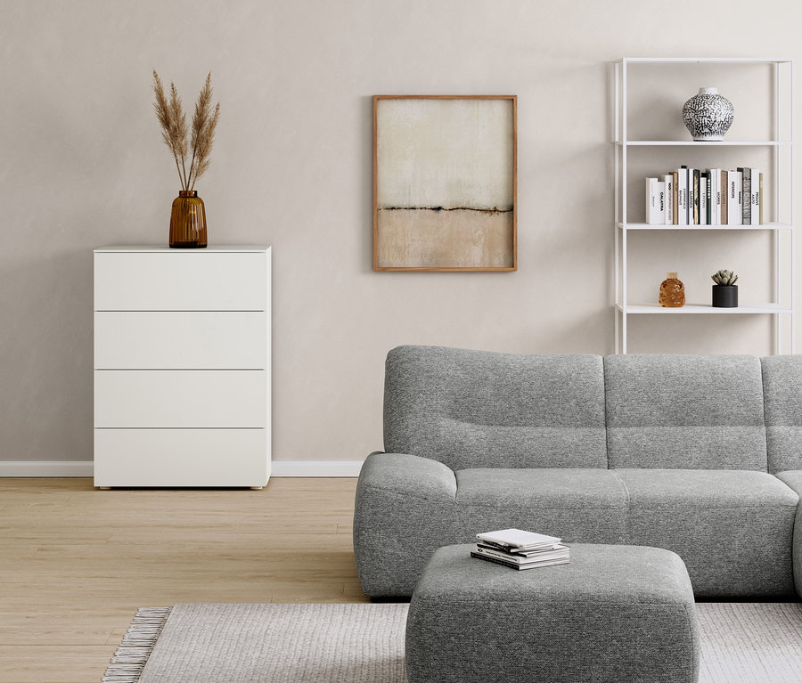 Im Zimmer stehen eine weiße Kommode mit Schubladen, ein Metallregal, ein graues Sofa und ein Hocker.