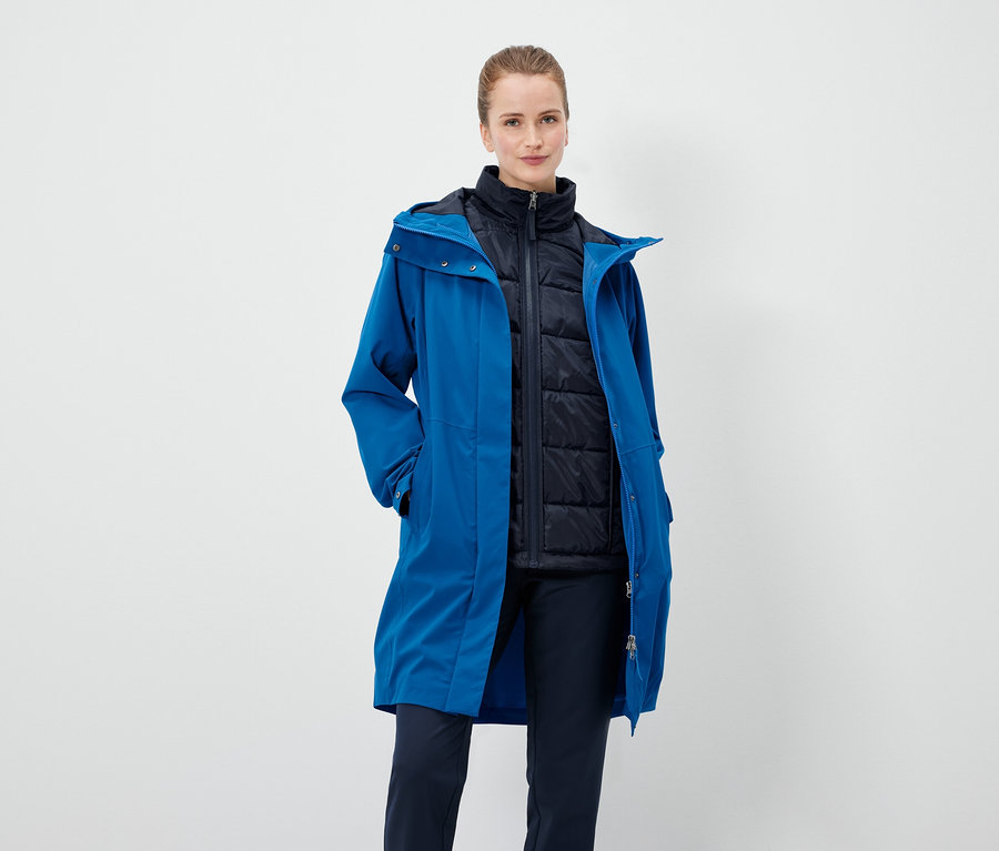 Eine Frau trägt einen blauen Mantel und eine schwarze Weste.