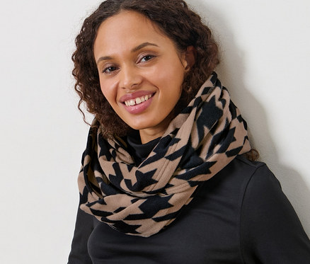 Frau mit braunen lockigen Haaren sitzt und trägt einen bedruckten Fleece-Loop mit Hahnentrittmuster.