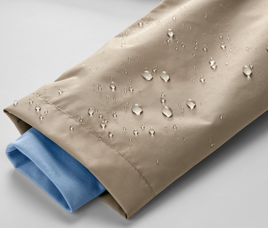 Detailaufnahme einer braunen Kinder-Regenjacke mit Wassertropfen und einem blauen Hemdsärmel.