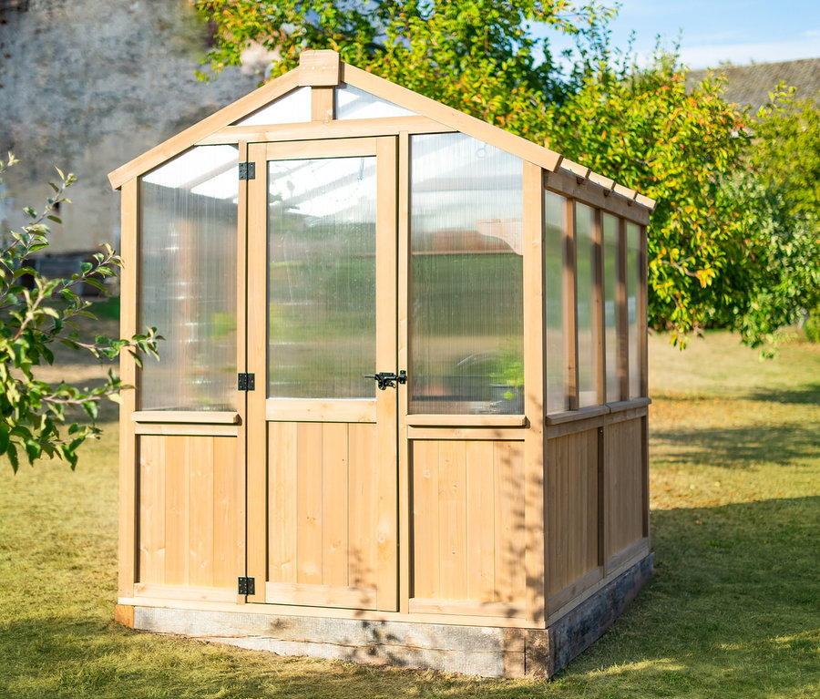 Kleines Gewächshaus aus Zedernholz steht auf Rasen.