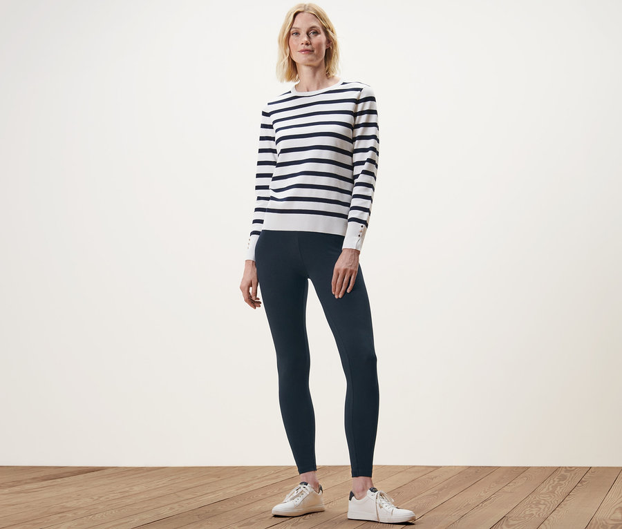 Frau posiert stehend in dunkelblauen Leggings und einem gestreiften Pullover.