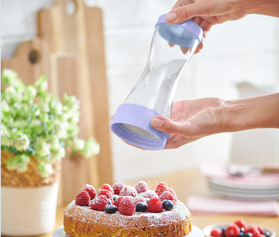 Eine Frau bestreut einen Kuchen mit Beeren mit einem Puderzuckerstreuer.