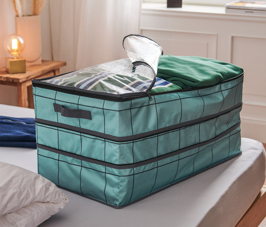 Eine Jumbo-Aufbewahrungstasche steht auf einem Bett und ist mit Kleidung gefüllt.