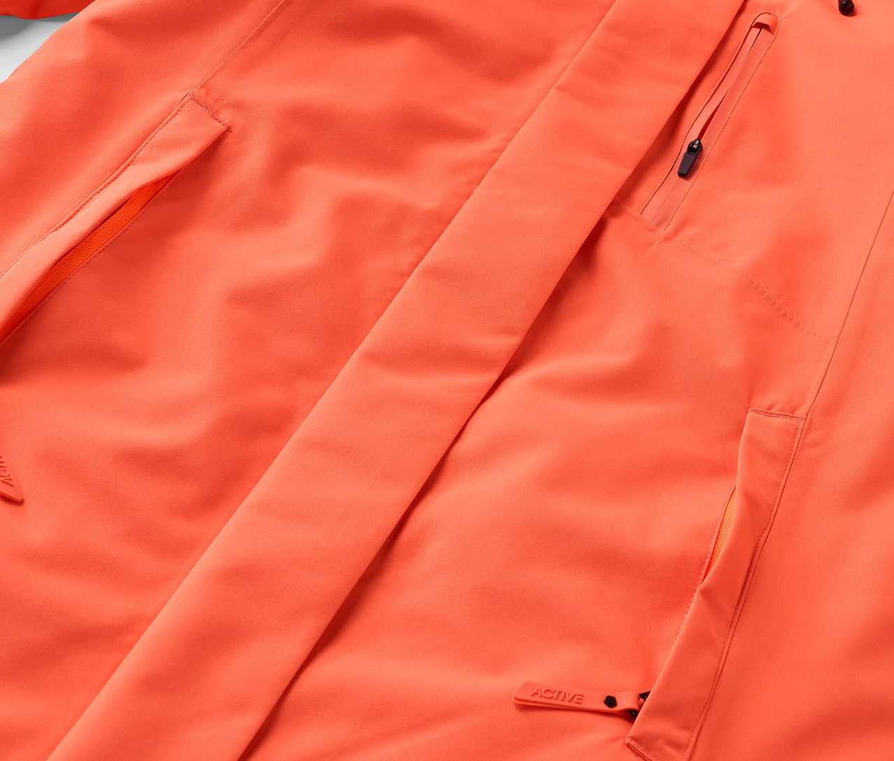 Detailansicht einer orangefarbenen Jacke mit Taschen und Reißverschluss.