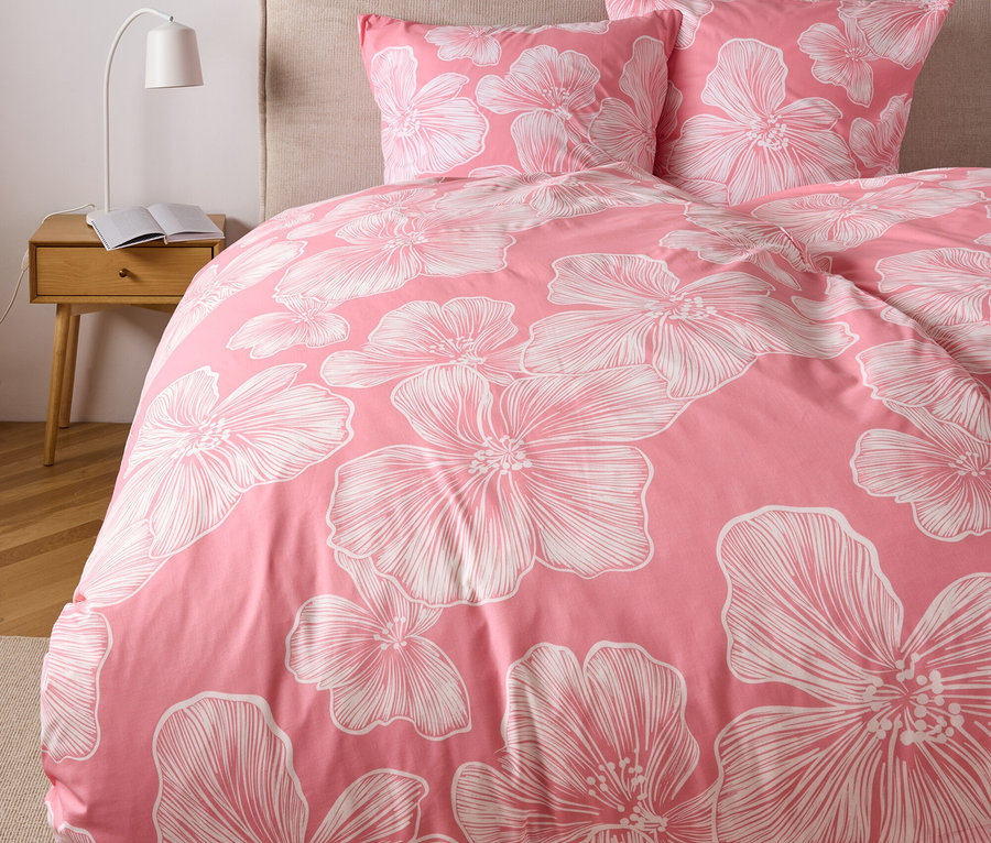 Nahaufnahme eines Bettes mit rosafarbener Polycotton-Bettwäsche mit weißen Blumenmustern, inklusive Kissen in Normalgröße und Übergröße.