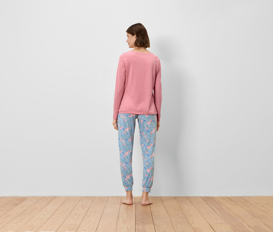 Frau mit dem Rücken zur Kamera trägt ein rosafarbenes Langarmshirt und eine blaue Hose mit Blumenmuster.