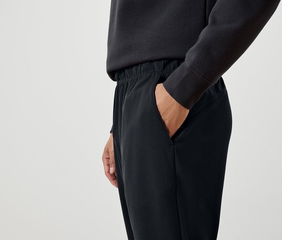 Mann mit Hand in der Tasche einer schwarzen Trainingshose.