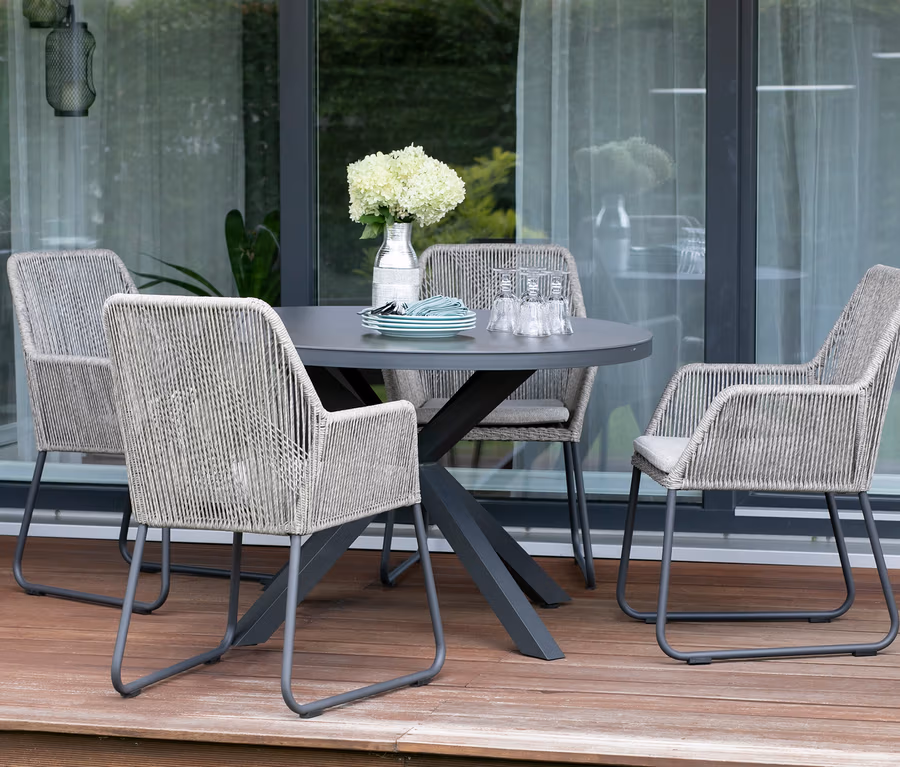 Vier deVries 2 Dining-Sessel um einen Tisch auf einer Terrasse.
