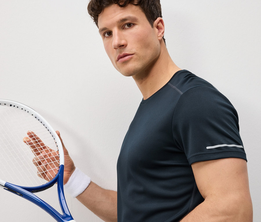 Mann hält Tennisschläger und trägt ein dunkelblaues Funktionsshirt.
