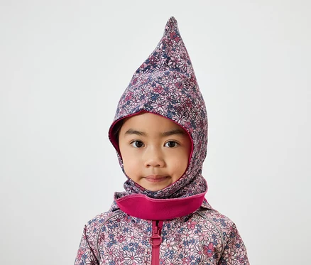 Porträt eines kleinen Mädchens mit braunen Augen in einer floralen Sturmhaube mit rosa Rand und Jacke.