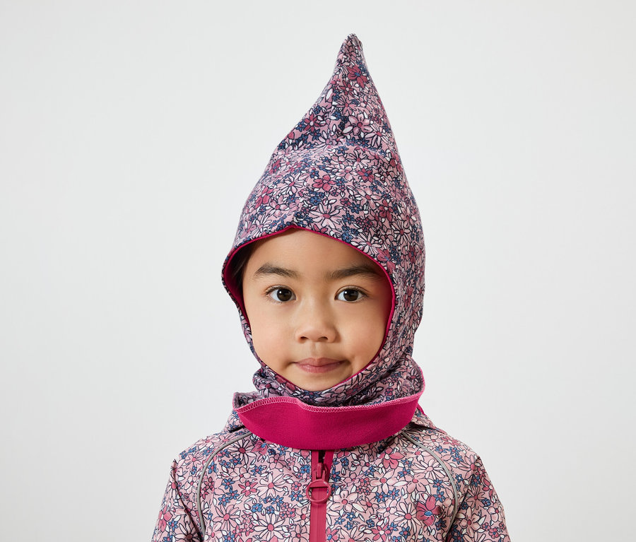 Porträt eines kleinen Mädchens mit braunen Augen in einer floralen Sturmhaube mit rosa Rand und Jacke.