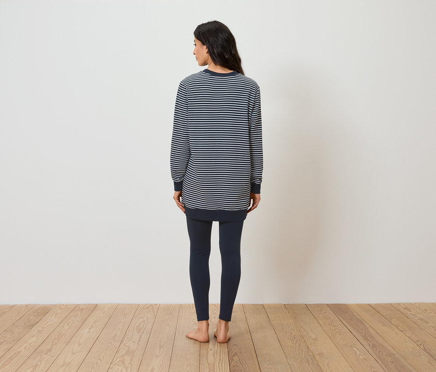 Frau steht mit dem Rücken zur Kamera und trägt ein gestreiftes Langarmshirt und Leggings.