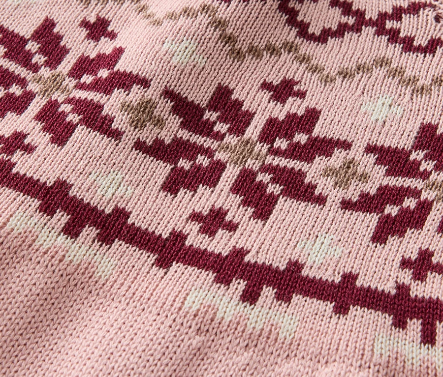 Detailaufnahme eines rosafarbenen Strickpullovers mit einem Muster aus bordeauxroten und beigen Schneeflocken.