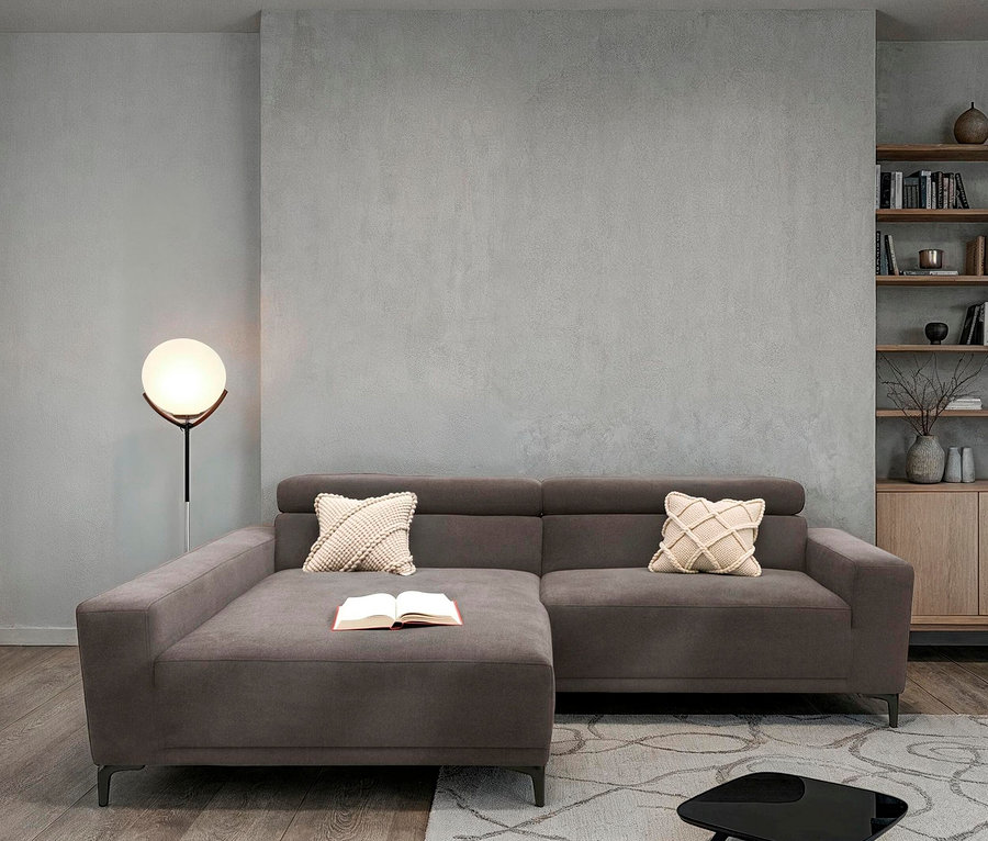 Wohnzimmer mit grauem Ecksofa, Kissen, Buch und Lampe.