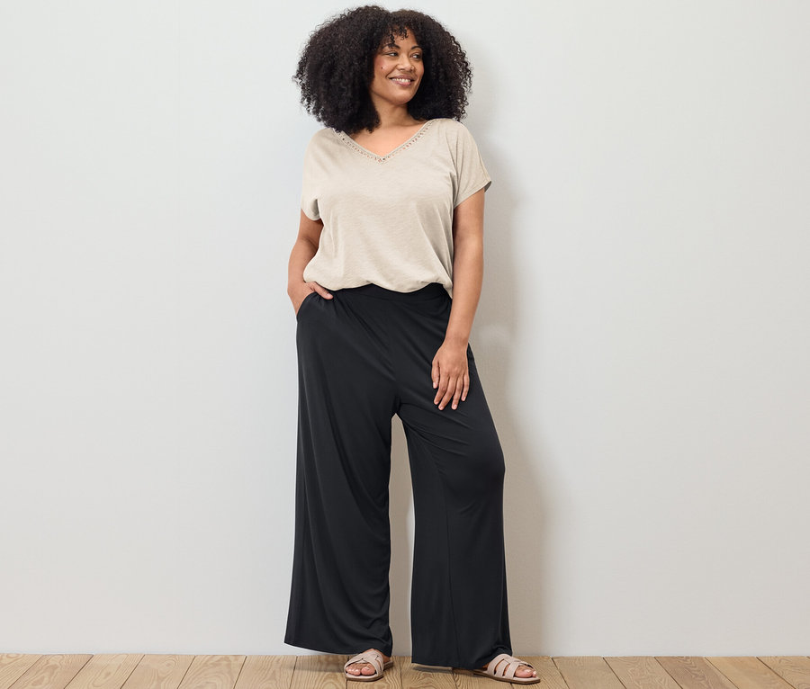 Frau posiert in einem cremeweißen Shirt aus Modalmix und einer schwarzen Palazzohose.