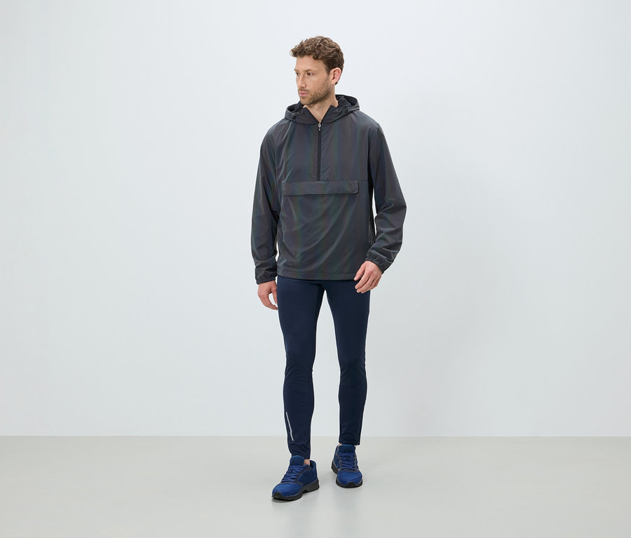 Mann steht und trägt eine graue Kapuzenjacke, dunkelblaue Leggings und blaue Schuhe.