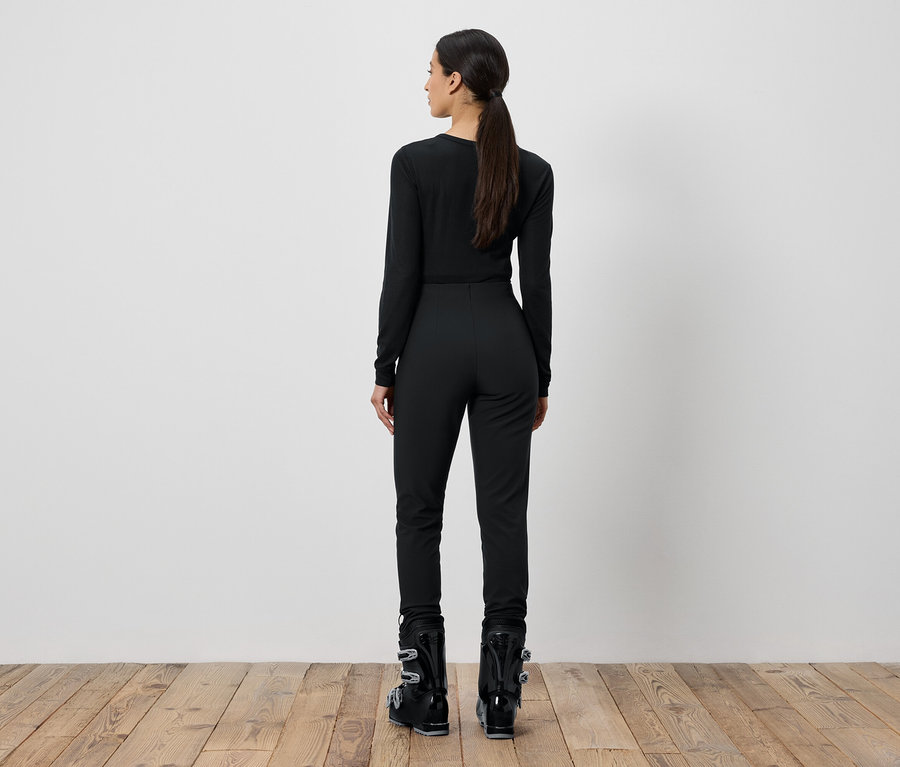 Frau in schwarzer Skibekleidung steht mit dem Rücken zur Kamera.