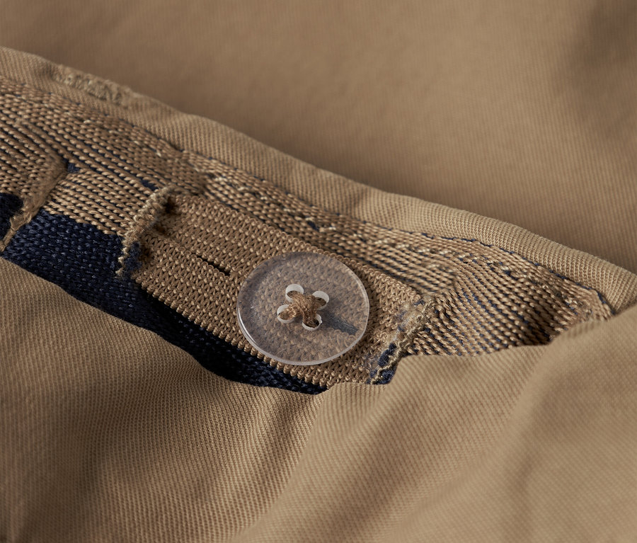 Detailaufnahme eines beigen Hemdes mit Knopf und dekorativem Band.