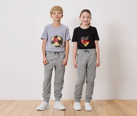 Ein Junge in einem grauen T-Shirt mit einem Fußball-Design und ein Mädchen in einem schwarzen T-Shirt mit einem Herz-Design, beide tragen graue Jogginghosen.