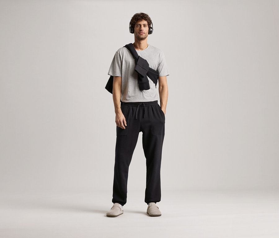 Mann mit Kopfhörern, grauem T-Shirt und schwarzer Sweathose.