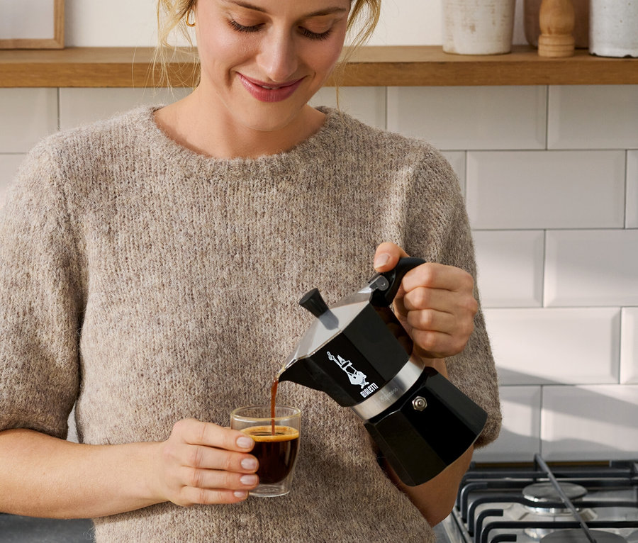 Frau giesst Kaffee aus einer schwarzen Bialetti Moka Express, 190 ml, in eine Tasse.