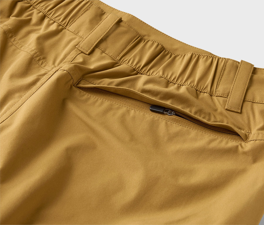 Detailaufnahme von khakifarbenen Hosen mit elastischem Bund und Reißverschlusstasche.