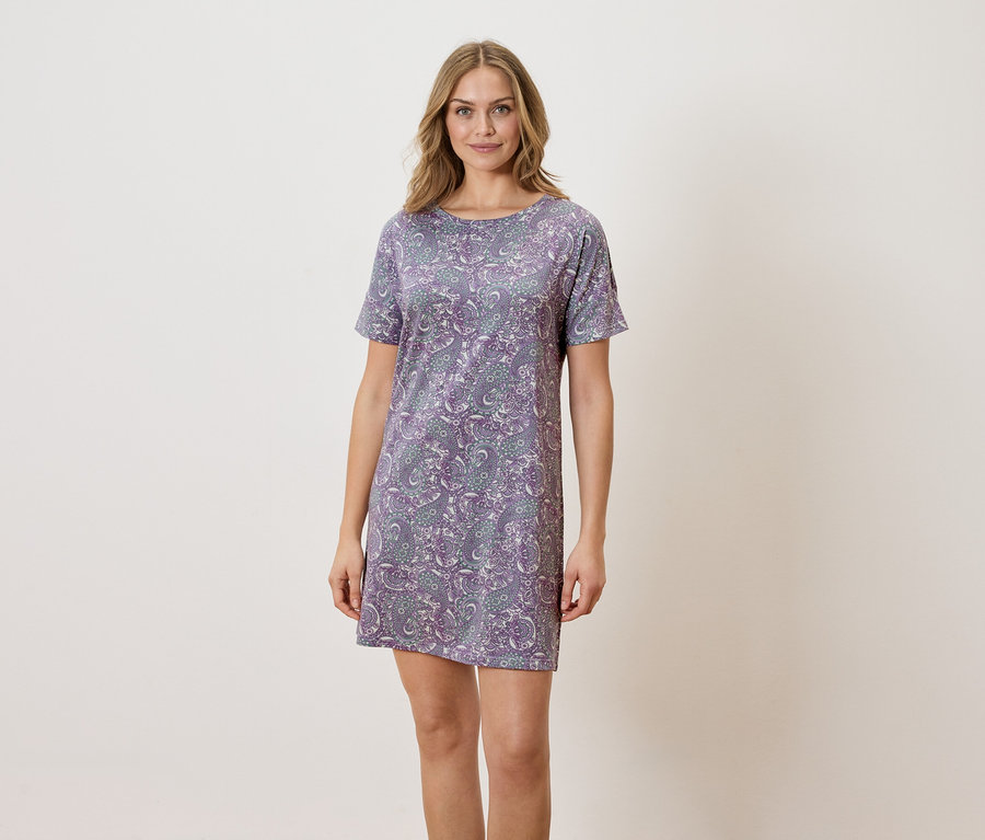 Frau steht und trägt ein lilafarbenes Kleid mit Paisley-Muster.