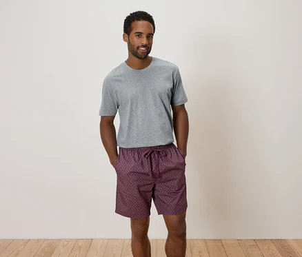 Mann steht mit verschränkten Händen in grauer Hose und gemusterten Shorts da.