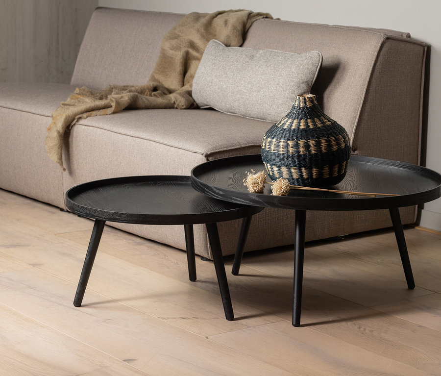 Vor beigem Sofa stehen zwei schwarze WOOOD »Mesa XL« Beistelltische aus Holz. Auf dem größeren Tisch steht eine Vase.