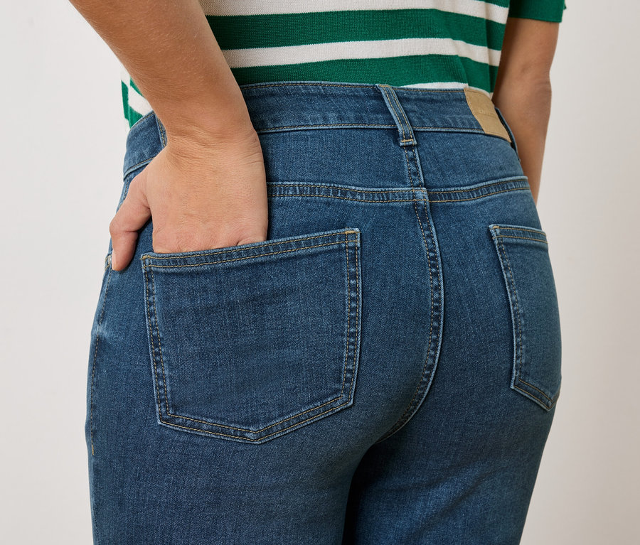 Nahaufnahme einer Person von hinten, die blaue Jeans und ein grün-weiß gestreiftes Oberteil trägt und die Hand in der Gesäßtasche hat.